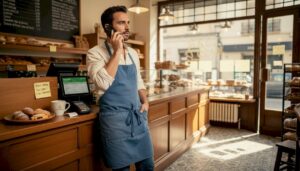 El dueño de la panadería atiende una llamada telefónica desde el mostrador mientras sigue pendiente de su negocio.